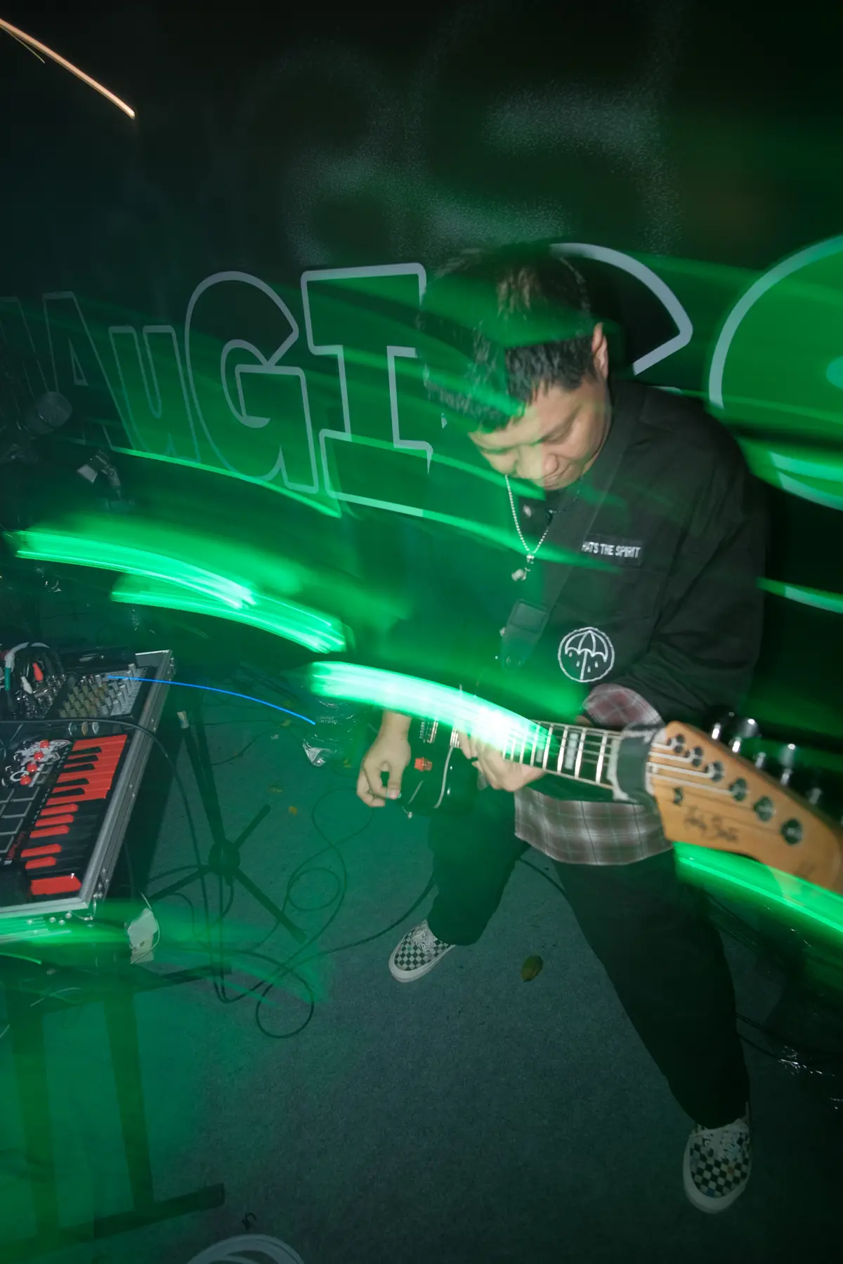 Welige playing guitar on stage, green light trails behind him